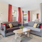 Wohnzimmer mit grauem Sofa, roten Vorhängen und Holztisch.