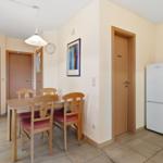 Essbereich mit Tisch, Stühlen und Kühlschrank. Tür führt in Schlafzimmer.