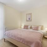 Schlafzimmer mit Bett, Nachttisch und Fenster mit weißen Vorhängen.