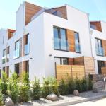 Moderne Wohnhäuser mit Holzverkleidung und Balkonen. Grünflächen und Steine im Vorgarten.