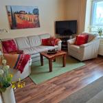 Wohnzimmer mit Sofa, Sessel, Fernseher und Holzboden.