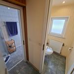 Badezimmer mit Dusche und Toilette. Holzregal und blauer Handtuchhalter sichtbar.