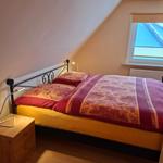 Schlafzimmer mit Dachschrägen, Bett mit gemusterter Bettwäsche und Holz-Nachttisch.