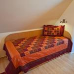 Schlafzimmer mit Dachschräge, Bett mit buntem Quilt und Holzboden.