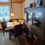 Esszimmer mit Tisch, Stühlen und Glasvitrine. Fenster mit Blick auf Außenbereich.