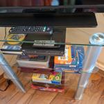 Glas-Tisch mit Fernseher, Fernbedienungen und Spielboxen auf mehreren Ebenen.