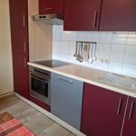 Küche mit roten Schränken, Edelstahlherd und weißen Fliesen.