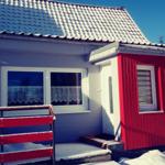 Ein Haus mit blauem und rotem Anstrich, Schnee auf Dach und Boden, weiße Fenster und eine Tür.