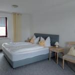 Schlafzimmer mit Doppelbett, Nachttisch, Stuhl und Fenster mit Jalousie.