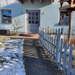 Haus mit blauer Fassade, Eingangstür und gepflastertem Weg mit Schnee.