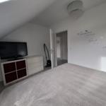 Schlafzimmer mit Dachschrägen, Bett, Fernseher und Wanddekoration.