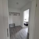 Flur mit grauem Boden und Blick in Schlafzimmer mit Bett.