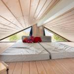 Bedroom with double bed under wooden roof, large window, toys on bed.