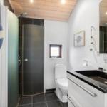 Bathroom with shower, toilet, and sink. Wooden ceiling and window.