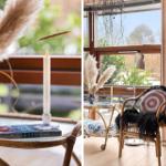 A room with rattan furniture, candles, and pampas grass by large windows.