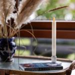 On a round table, there is a book, a candle, and a plant in a blue pot.