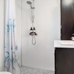 Bathroom with shower, sink, and toilet. Tiled wall and shower curtain with floral pattern.