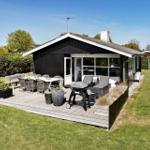Black house with terrace, grill, and garden furniture. Surrounded by greenery.