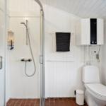 Badezimmer mit Dusche, Toilette und Heizung. Fliesenboden und weiße Wände.