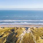 Ausblick auf Strand und Meer mit Dünen im Vordergrund.