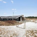 Ein schlichtes Haus mit Dach und Fenstern steht auf einer sandigen Fläche mit einem Fußballtor.