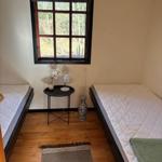 Two sleeping areas with mattresses, small table, and window with view of forest.