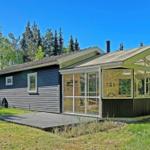 Modern cabin with glass porch and wood siding in a green setting.