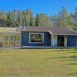 A dark blue wooden house with a terrace and glass veranda in the green.