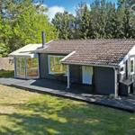 A house with wooden deck, glass enclosure, and tiled roof surrounded by trees.