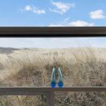 Durch das Fenster blickt man auf eine Wiese mit hohem Gras und zwei blauen Vasen.