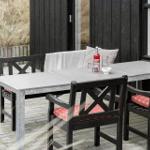 Terrasse mit Tisch und Stühlen, rote Sitzkissen, Getränke und Blick auf Gras.