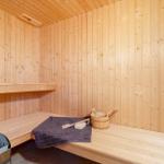 Sauna mit Holzbank, Holzwand und Holzdecke. Dampfstein, Eimer und Handtuch sind vorhanden.