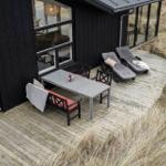 Terrasse mit Tisch, Stühlen und Liegen neben schwarzem Haus