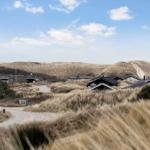 Häuser unter sanddünen mit steinweg und blauem himmel.