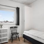 Schlafzimmer mit Bett, Stuhl und Fenster. Weißer Schrank und Holzboden.