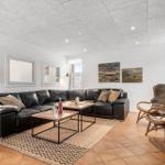 Wohnzimmer mit schwarzer Ledercouch, zwei Holztische und zwei Rattanstühle mit Felldecken.