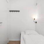 Ein schlichtes Schlafzimmer mit weißem Bett, Wandlampe und Kleiderhaken.