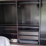 Großer Kleiderschrank mit Haken, Regalen und Schubladen. Bett ist teilweise sichtbar.