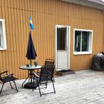 Terrasse mit Tisch, Stühlen und schwedischer Flagge vor einem Haus mit Wellblechfassade.