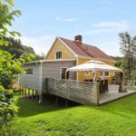 Haus mit Terrasse, Sonnenschutz und Garten. Umgeben von Bäumen und Gras.