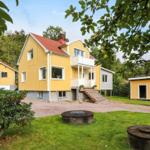Gelbes Haus mit Balkon und Garten. Zwei kleinere Häuser und Bäume sind sichtbar.
