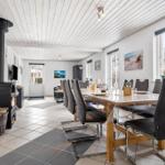 Dining room with wooden table, chairs, and wood stove. White walls and large windows.