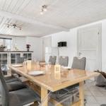 Dining area with wooden table, chairs, and wood stove. White walls and ceiling.