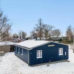 Blue wooden shed covered in snow, surrounded by trees and other buildings.