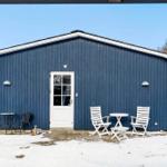 Blue wooden house with white door and outdoor table with chairs in snow.