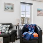 Living room with leather sofa, armchair, and windows. Wall art shows beach.