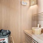 Sauna with wooden bench, wooden bucket, and thermostat on the wall.
