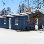 Blue wooden house with white door and windows. Snow covers the ground around the house.