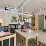 Wohnzimmer mit Sofa, Couchtisch und Kaminofen. Holzwände und -decke. Treppenhaus im Hintergrund.