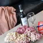 Auf dem Tisch steht eine Weinflasche, ein Glas, ein Sudoku und eine Vase mit Hortensien.